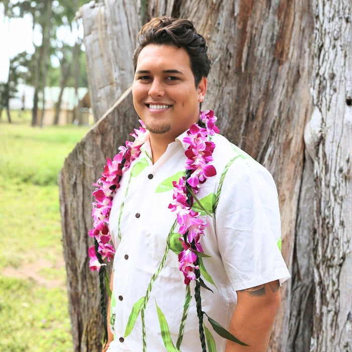 Man wearing a white shirt with ti leaf lei & purple orchid wrap.